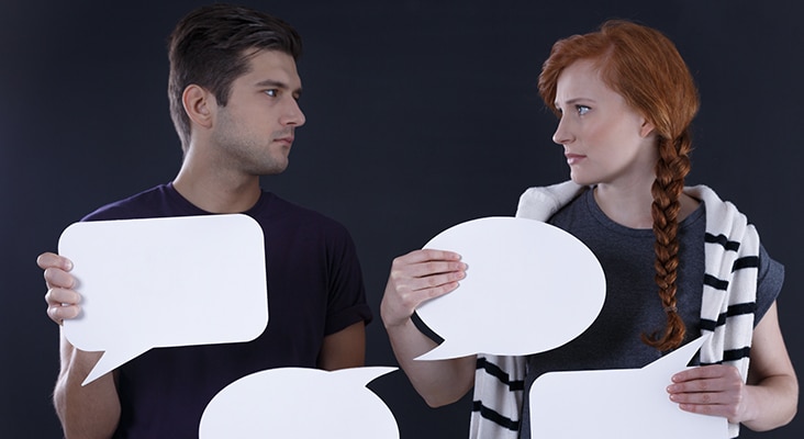 Young couple holding blank speech bubbles, dark background