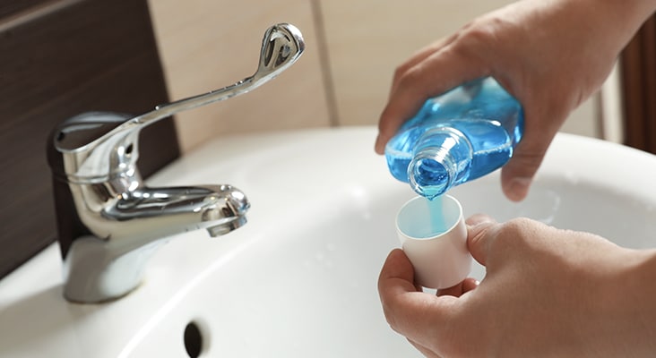 Man pouring mouthwash from bottle into cap in bathroom, closeup. Teeth care