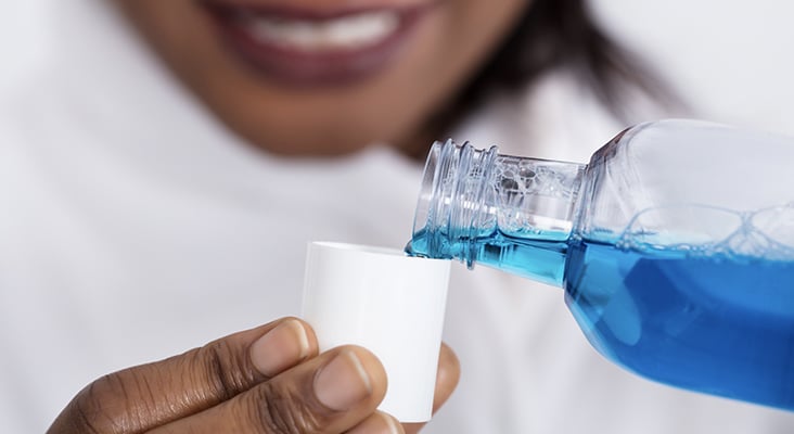 Close-up Of A Human Hand Pouring Mouthwash Into Bottle Cap