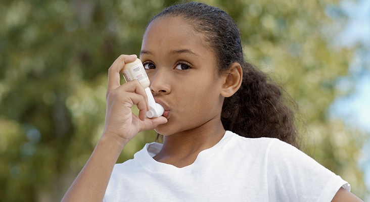 Girl (7-9) using inhaler, outdoors