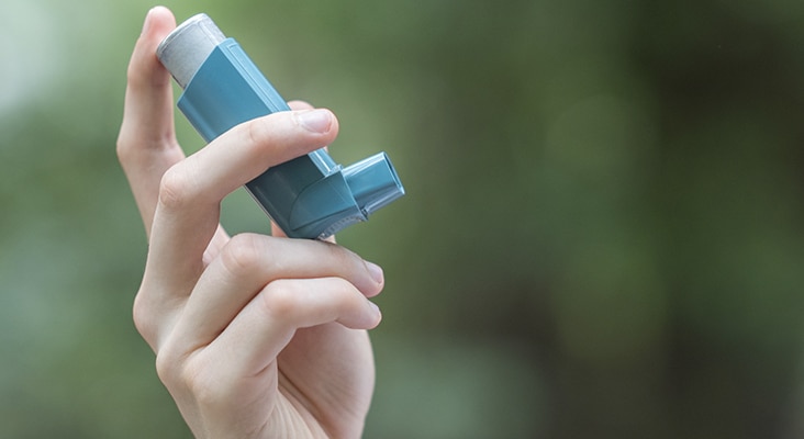 View of a man's hand holding a blue asthma inhaler