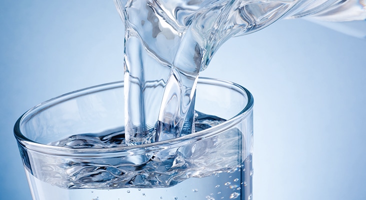 Pouring water from jug into glass on blue background