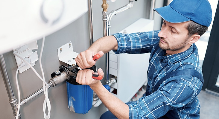 Young man in workwear using pliers while installing water filtration system