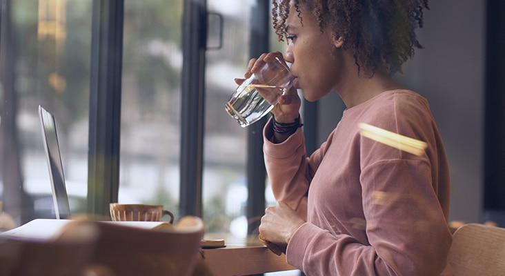 side view of one pretty young black woman study working indoor with laptop drinking water