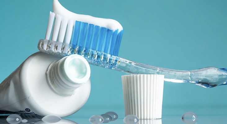 New toothbrush with toothpaste close-up in the bathroom on a mirror table with water drops on a blue background in the sunlight