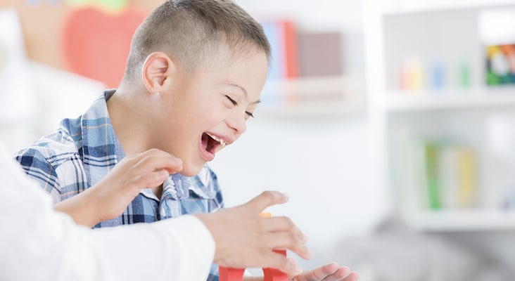 Cheerful preschool age boy enjoys playing with blocks with his teacher.