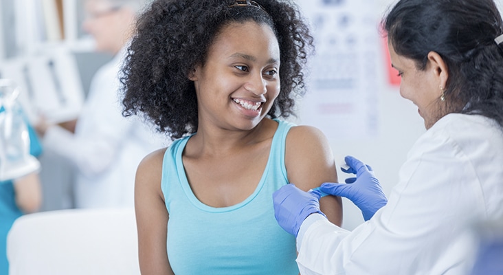 Female doctor puts a bandage on teenage girl's arm after receiving immunization.