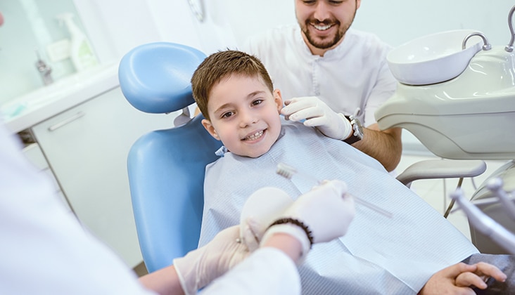 dentist showing young boy how to properly brush teeth