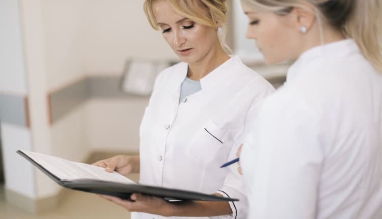 Two women doctors standing with clipboard at hospital and discussing cases