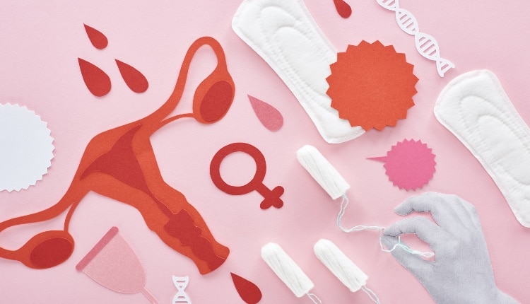 cropped view of white hand holding tampon on pink background with sanitary napkins, paper cut female reproductive internal organs and blood drops