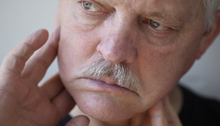 Senior man touches his sore jaw area.