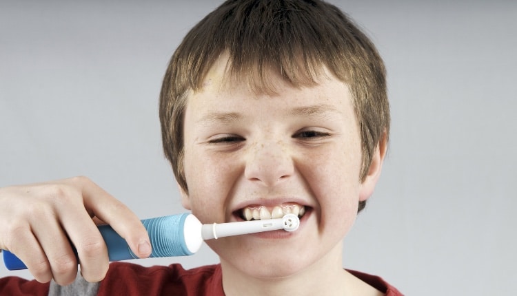 Boy aged 12 to 13 years brushing teeth with electric toothbrush