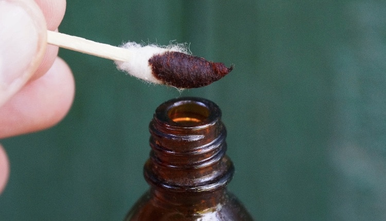 fingers hold a wand with a cotton swab in brown iodine over an open opened bottle