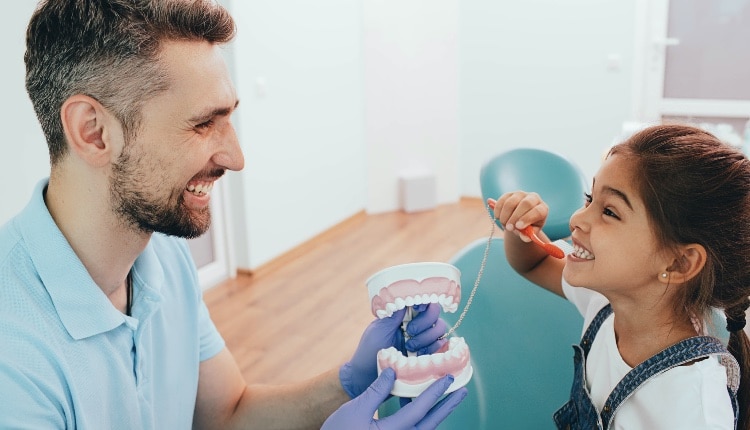 Laughing little girl showing how to brush teeth to her dentist, during a dental appointment