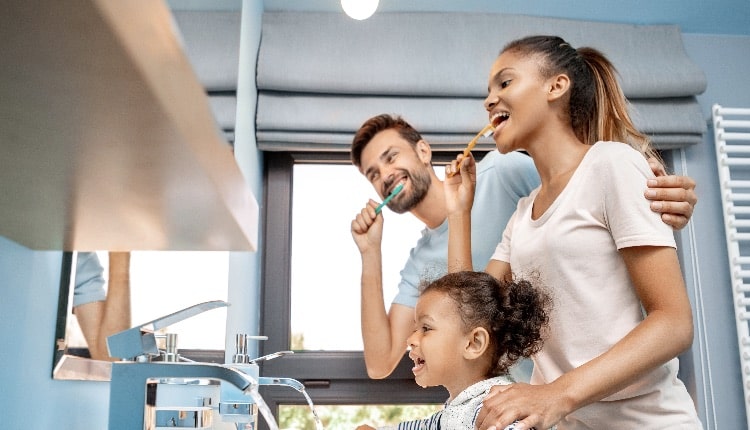 Mother, father and daughter brushing teeth in bathroom