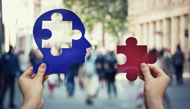 Two hands holding a paper with human head and a puzzle piece.