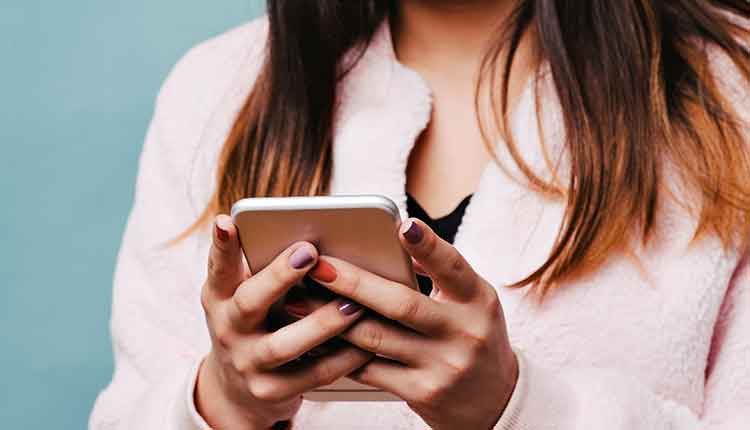 Teen Female Texting on a Smart Phone with Solid Blue Background and Pink Fur Jacke