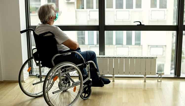 Senior man in wheelchair looking through the window during COVID-19 lockdown