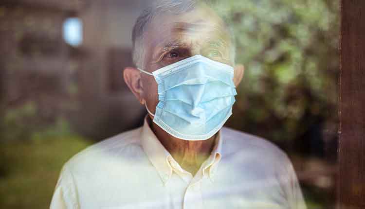 Senior man stays home because of Corona virus. He stands by the window and looks out at the garden