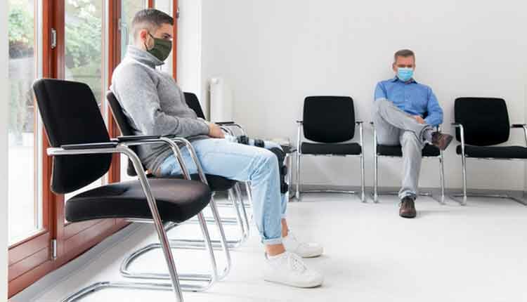 Young and mature man with face masks sitting in a waiting room of a hospital or office