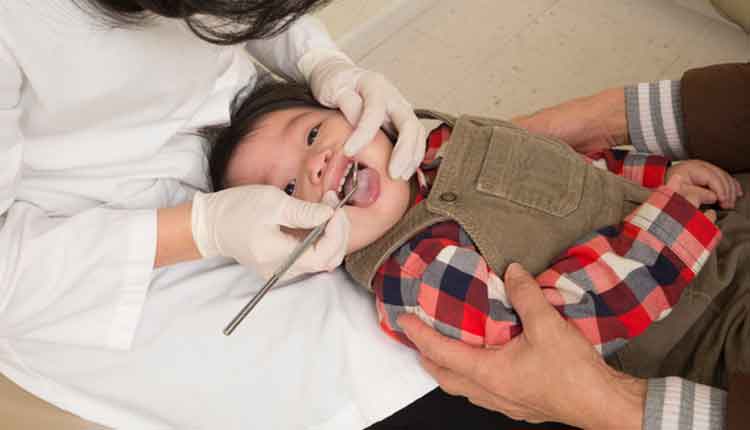 1 Year old's first dentist appointment. This is the proper position for a baby's dental check-up - baby's head is in dentist's lap knee-to-knee with mom who is holding on.