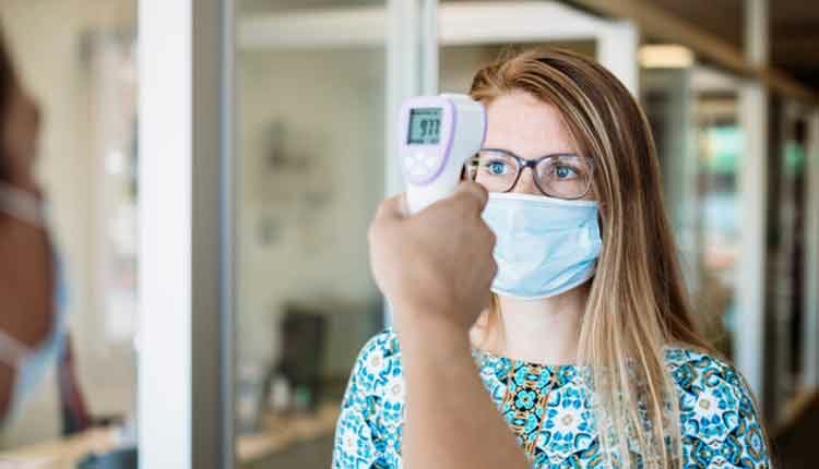 Woman Has Temperature Taken By Office Worker Wearing Mask