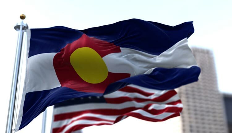 the flag of the US state of Colorado waving in the wind with the American stars and stripes flag blurred in the background