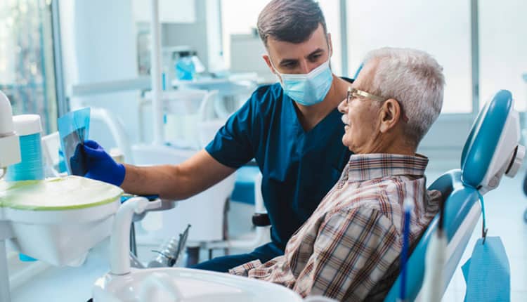 Senior man sitting in a dental chair while his dentist reads him out an x-ray scan