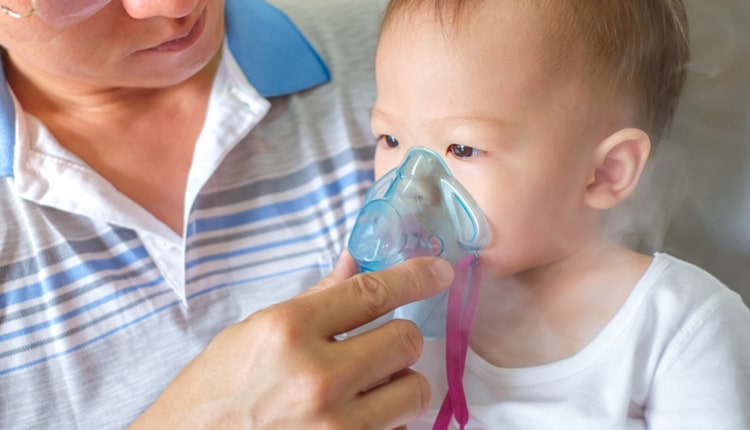 Sick little kid with respiratory problem with oxygen mask breathes through nebulizer at doctor clinic