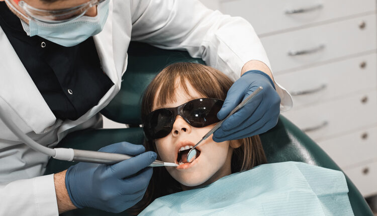 People, medicine, stomatology, technology and health care concept. Male dentist working with little girl in clinic.