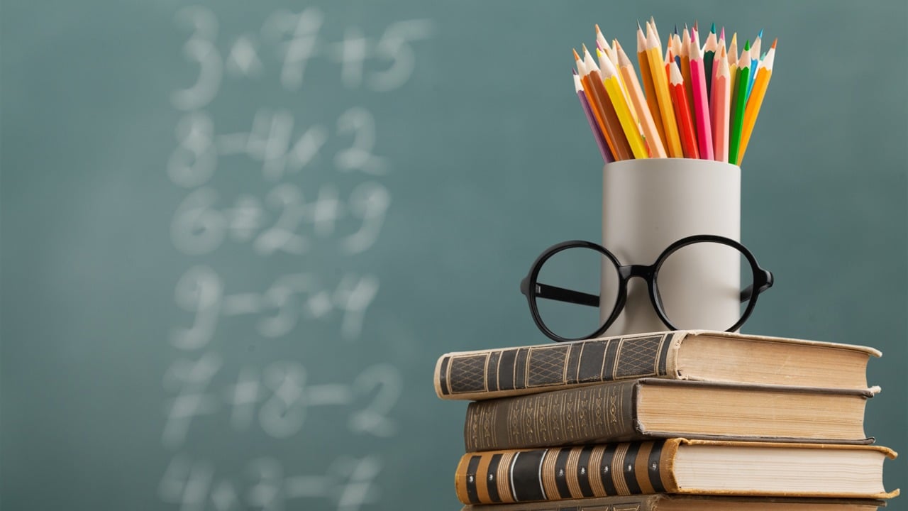 Books, eyeglasses, and colored pencils in front of a chalkboard