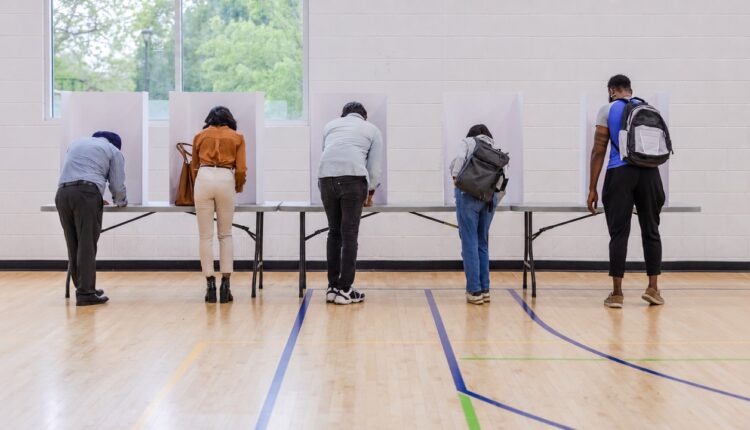 Five voters completing ballots at privacy partitions in a polling place
