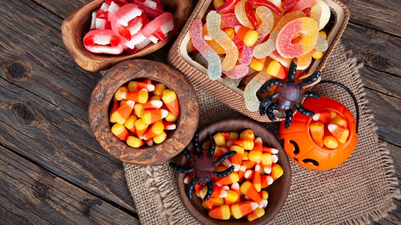 Bowls of candy corn and gummy sweets with Halloween spiders and a jack-o-lantern on a rustic table