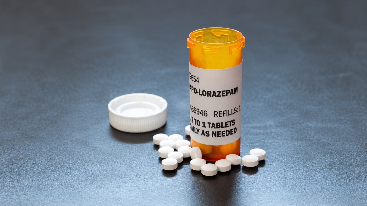 Amber lorazepam prescription bottle with white cap and tablets on a gray surface